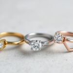 Three gold engagement rings in yellow, white, and rose gold displayed side by side showing their distinct color differences
