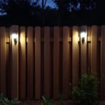 Illuminated wooden fence with solar lights creating a warm ambiance in a backyard garden at dusk
