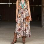 Elegant western wedding guest outfit featuring a woman in a floral maxi dress with cowboy boots and western accessories