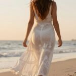 Woman wearing a white crochet maxi dress walking on beach at sunset