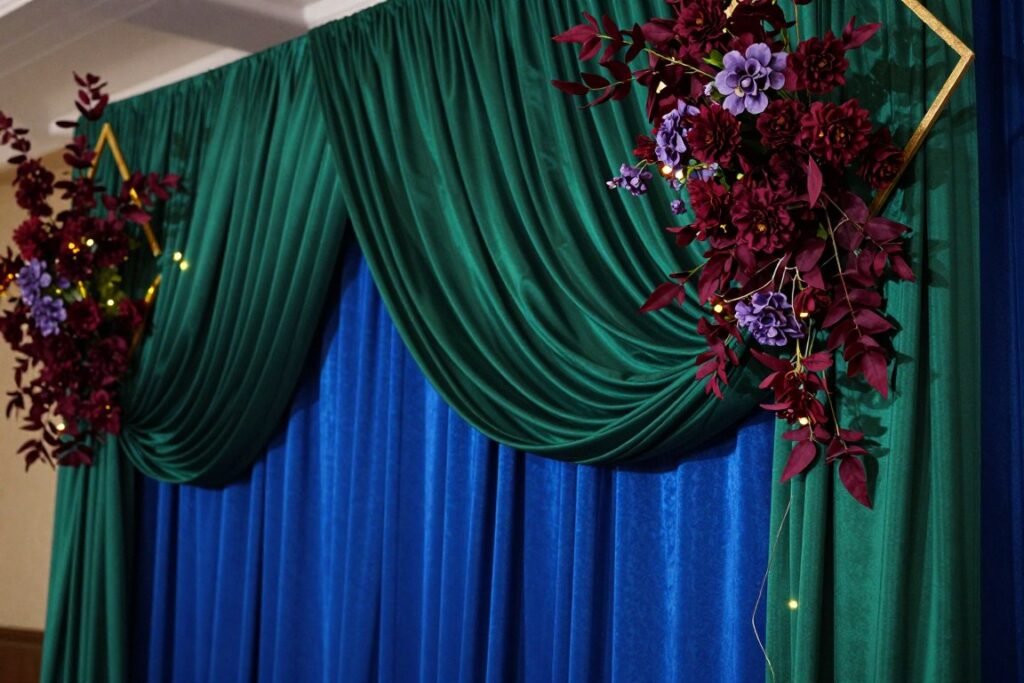 Close-up of jewel tone ceremony backdrop with draped fabric and floral elements Close-up of jewel tone ceremony backdrop with draped fabric and floral elements