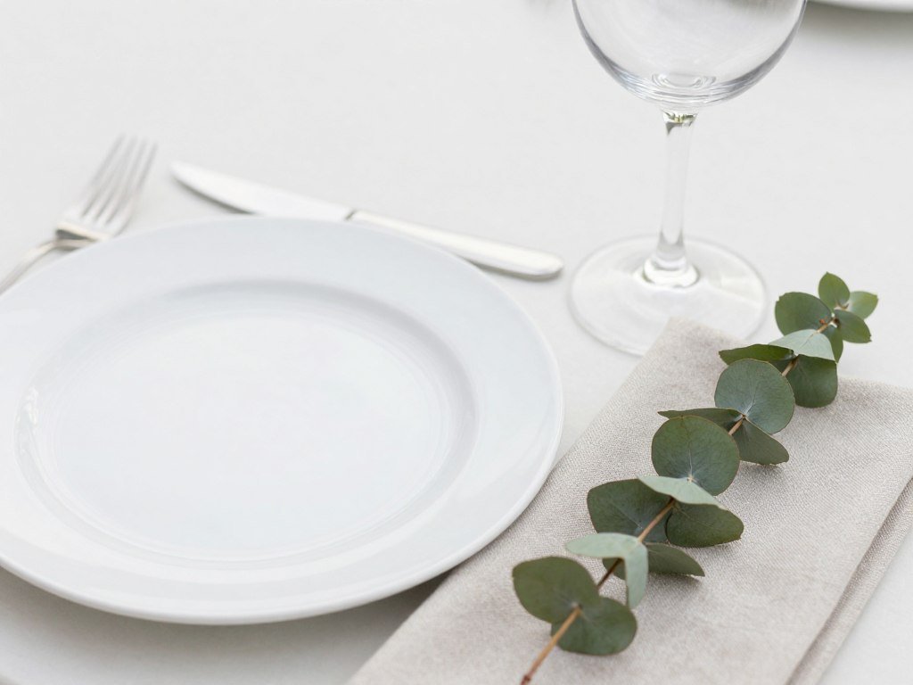 Close-up of minimalist place setting with simple white plate, elegant flatware, and clear glassware