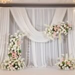 Backdrop Decorations: Creative Ideas for Stunning Event Backgrounds Elegant wedding backdrop decoration with white fabric and floral arrangements