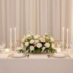Elegant wedding head table with white linens, floral centerpieces, and candles