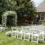 elegant backyard wedding ceremony setup with white chairs and floral arch
